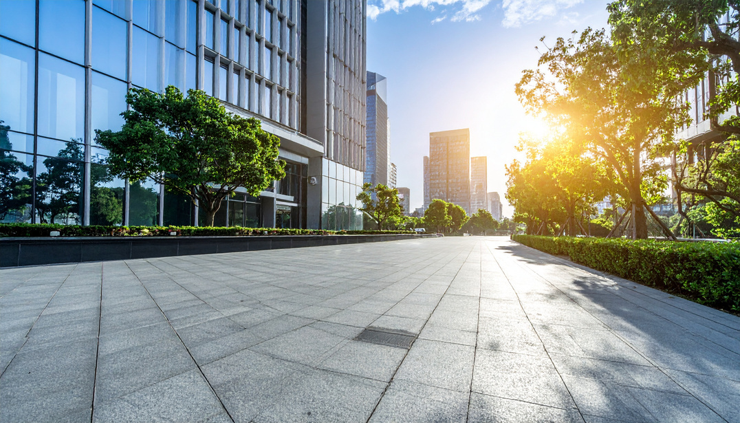 A modern corporate plaza with glass office buildings and trees at sunrise